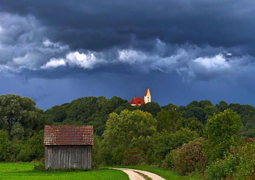 Blick auf die Burger Kirche - schwere Gewitterwolken hängen am Himmel und bevor sich die Sonne geschlagen gibt, taucht sie das Mindeltal in ein besonders stimmungsvolles Licht. (20.9.22.)